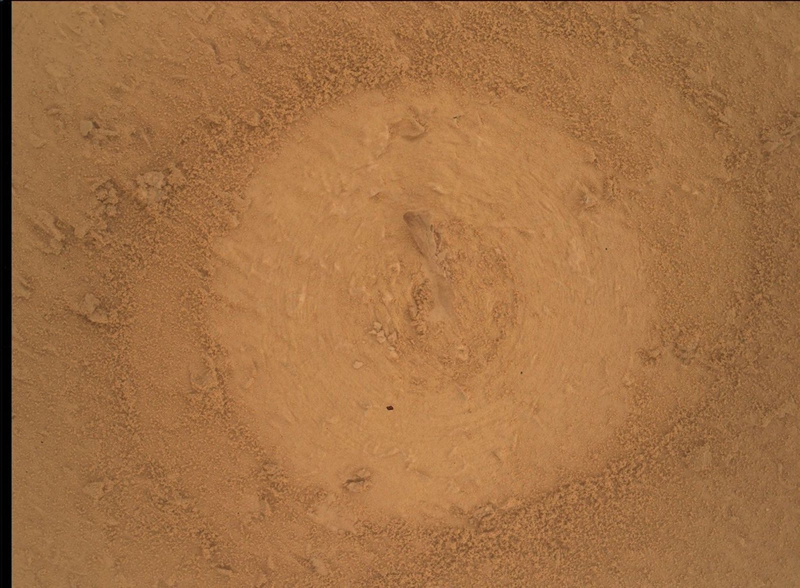 Close-up of the Basque Lakes rock target shows a lighter circular brushed area surrounded by reddish-brown grains and small fragments.