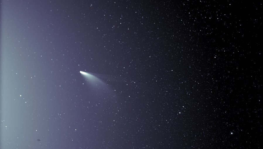 Comet NEOWISE appears against a star field with a broad pale dust tail and a thinner ion tail extending to the right.